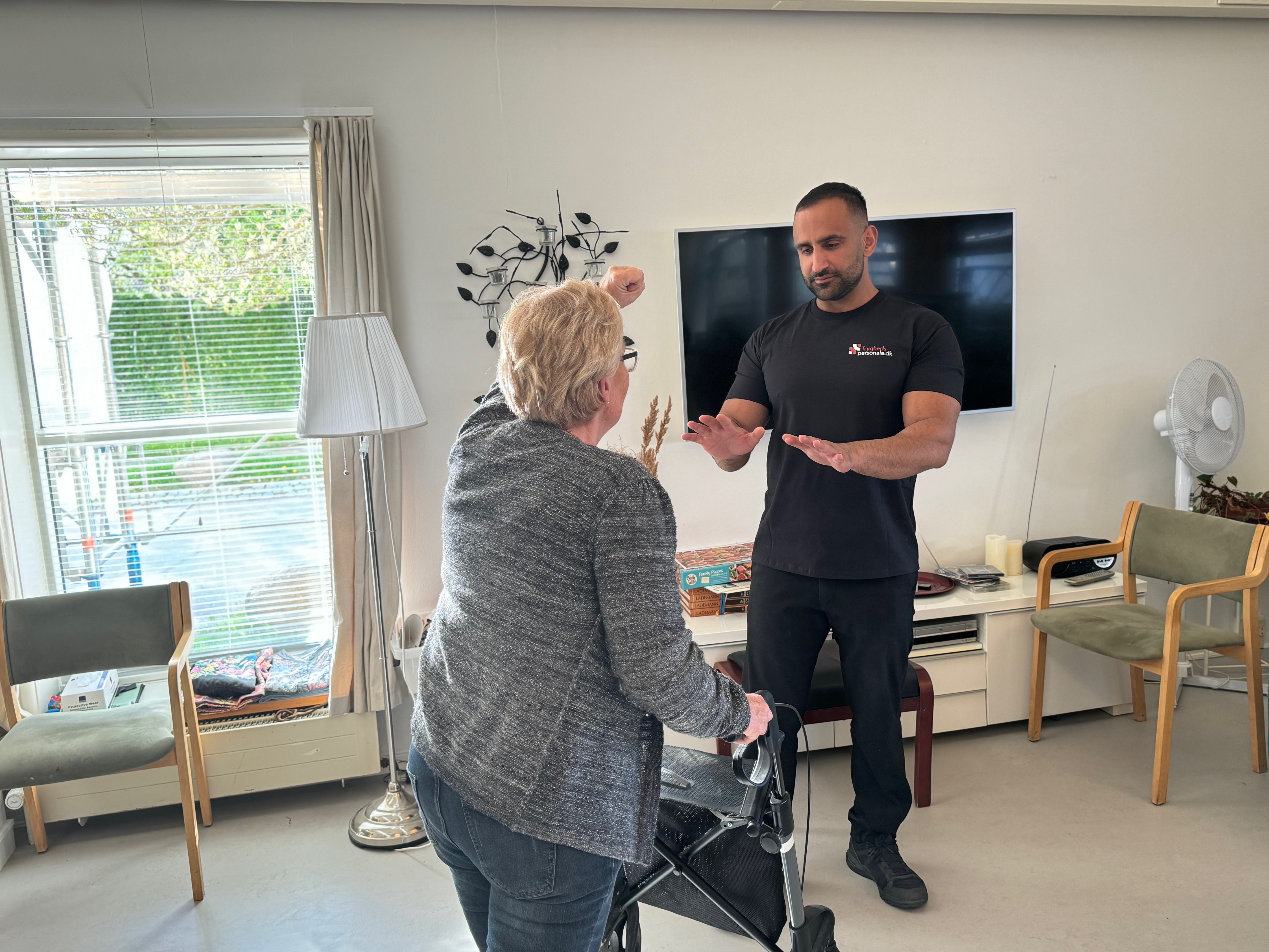 Sikkerhedsassistent i samtale med ældre dame med rollator på plejehjem